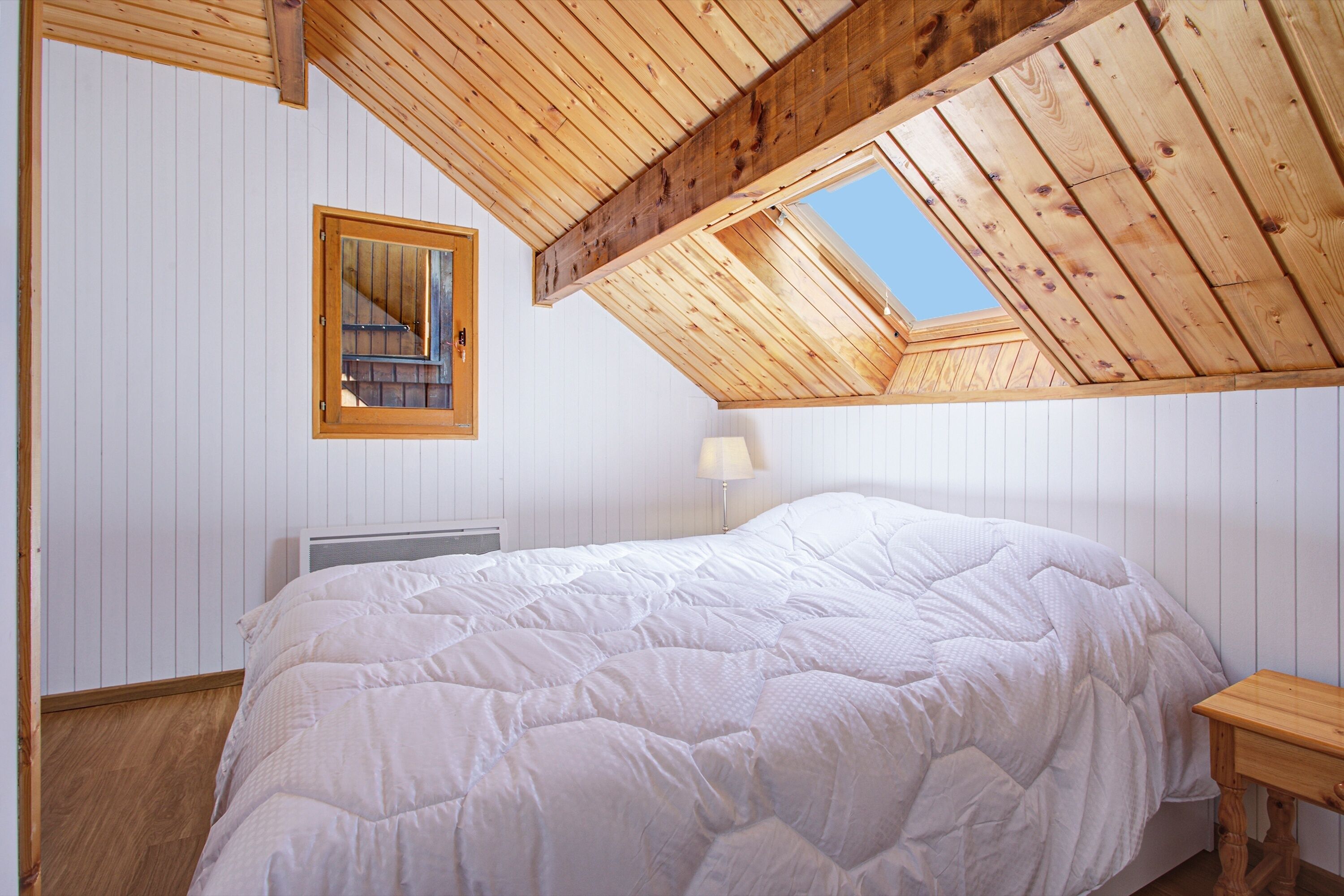 Une chambre avec un plafond en pente, un grand lit, une table de chevet, une lampe et une fenêtre.