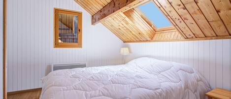 Une chambre avec un plafond en pente, un grand lit, une table de chevet, une lampe et une fenêtre.