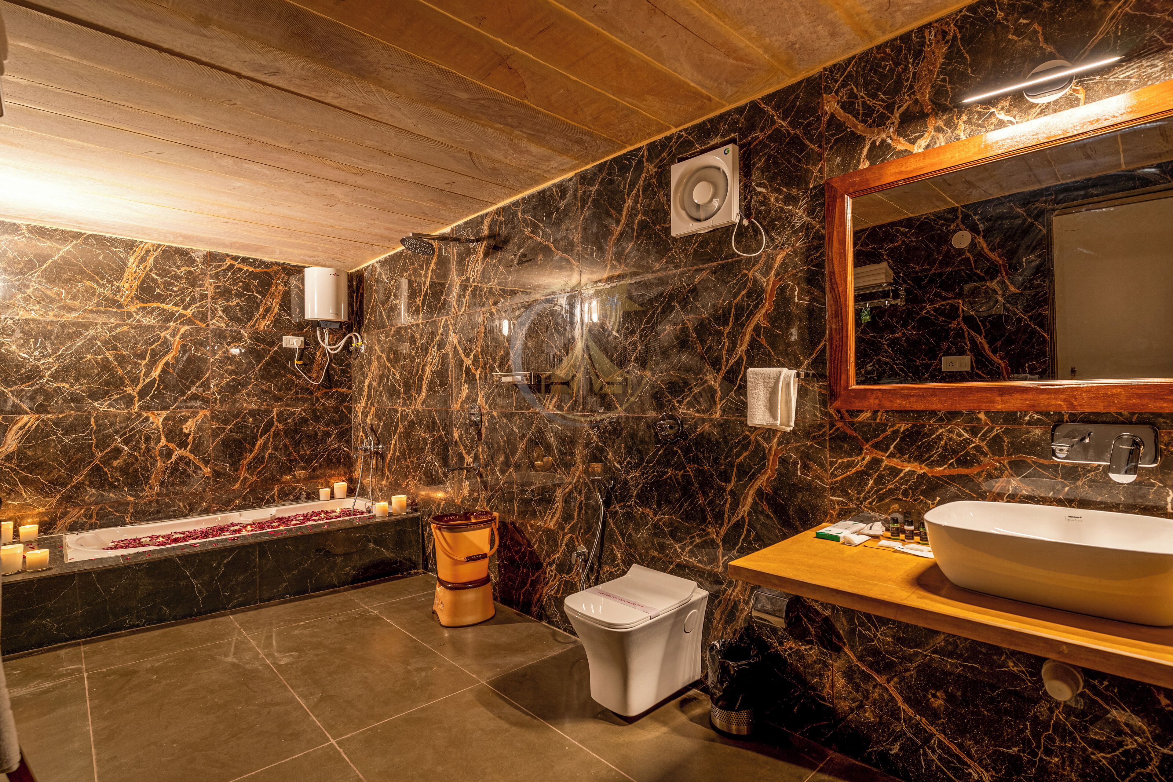 A bathroom with a marble wall, a wooden ceiling, a large mirror, a sink, and a bidet.