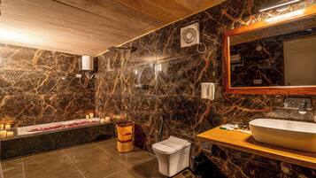 A bathroom with a marble wall, a wooden ceiling, a large mirror, a sink, and a bidet.