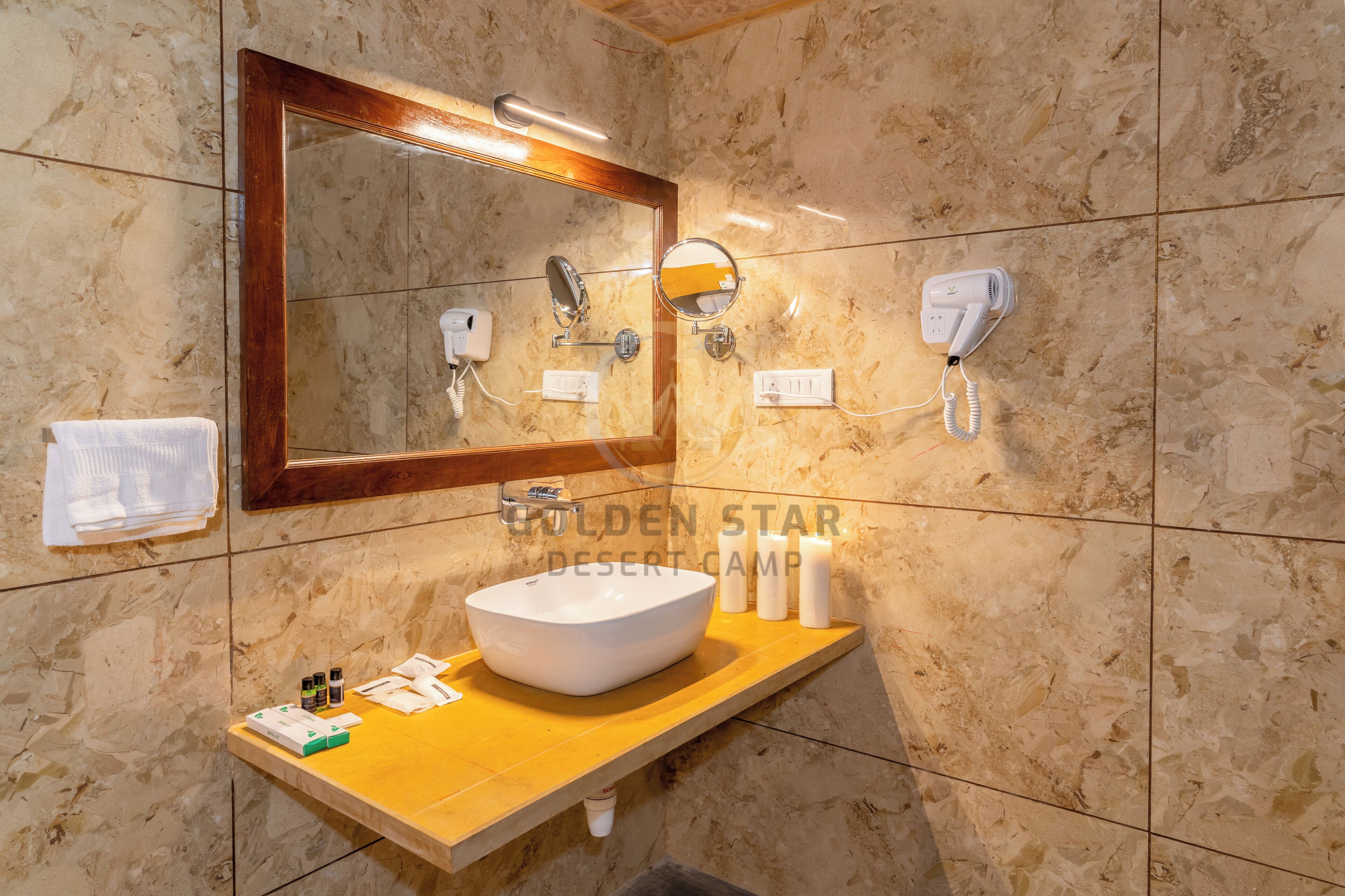 A bathroom with a marble wall, a wooden vanity, a large mirror, a sink, and a hairdryer.