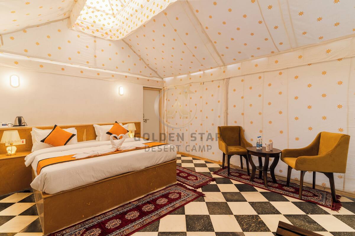 Een hotelkamer met een geruit vloertje, een bed met oranje en witte beddengoed, een klein rond tafeltje met stoelen, en behang met een patroon.