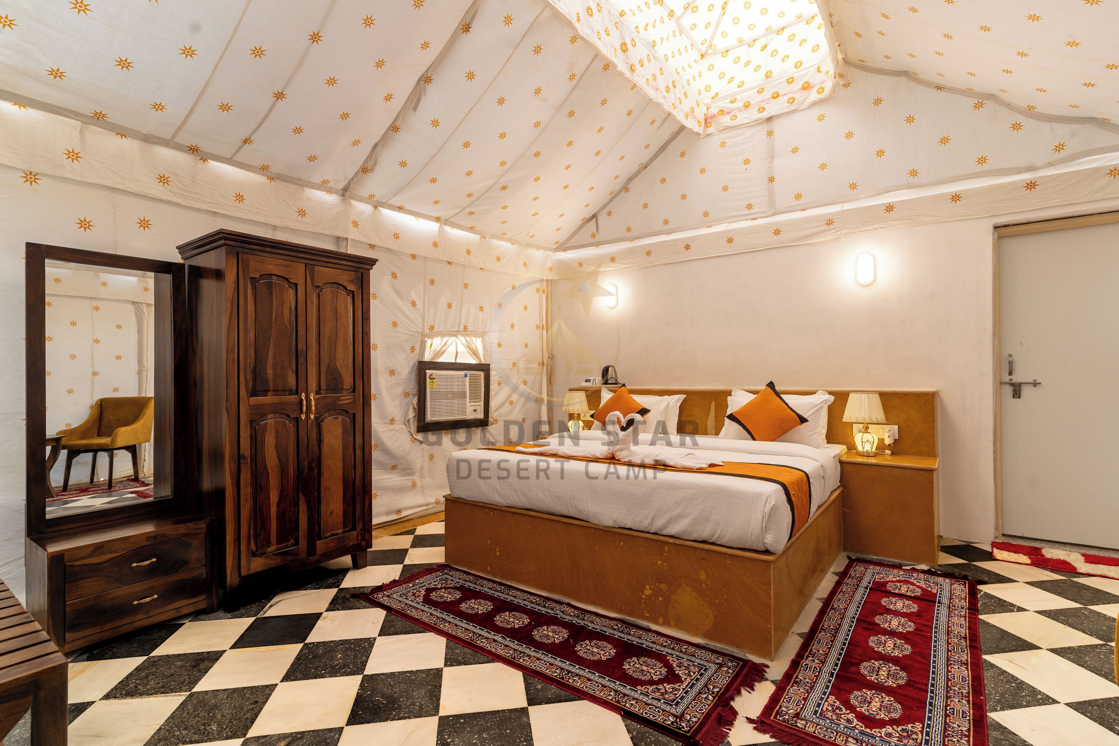A bedroom with a checkered floor, a bed with white and orange bedding, a wooden wardrobe, a mirror, and a patterned rug.