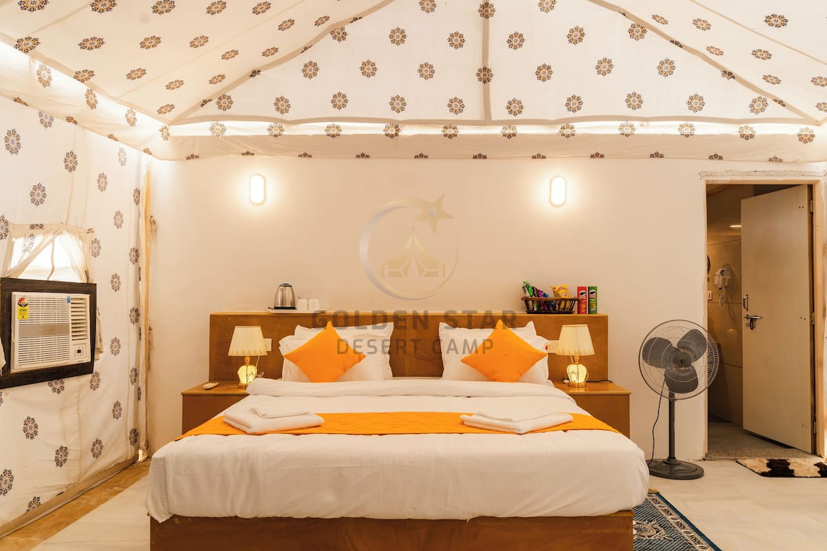 Hotelkamer met een bed, twee nachtkastjes met lampen, een wandairconditioner, een plafondventilator en een deur die naar een andere kamer leidt.