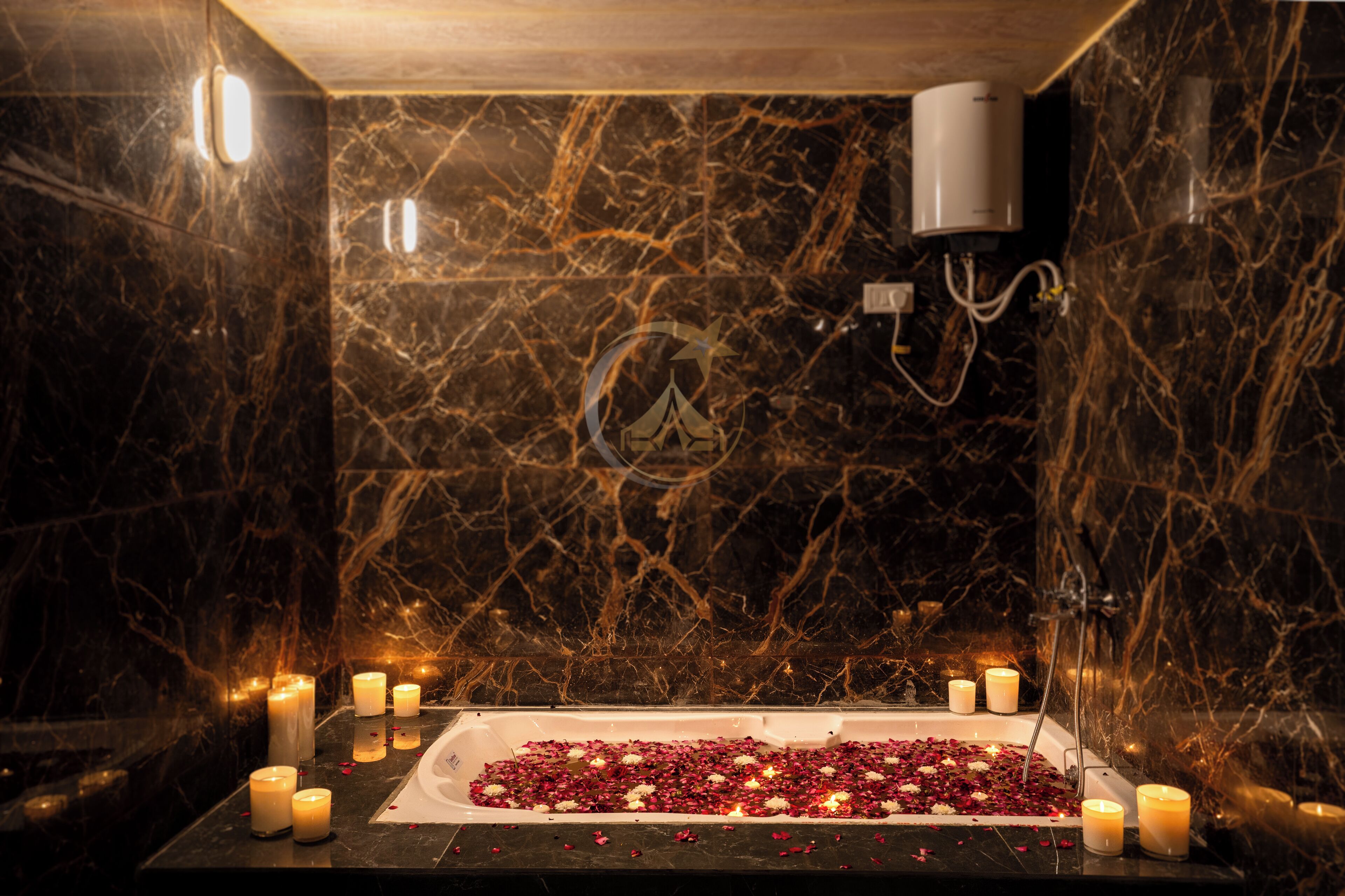 A bathroom with a marble wall, a bathtub filled with rose petals, and several lit candles.