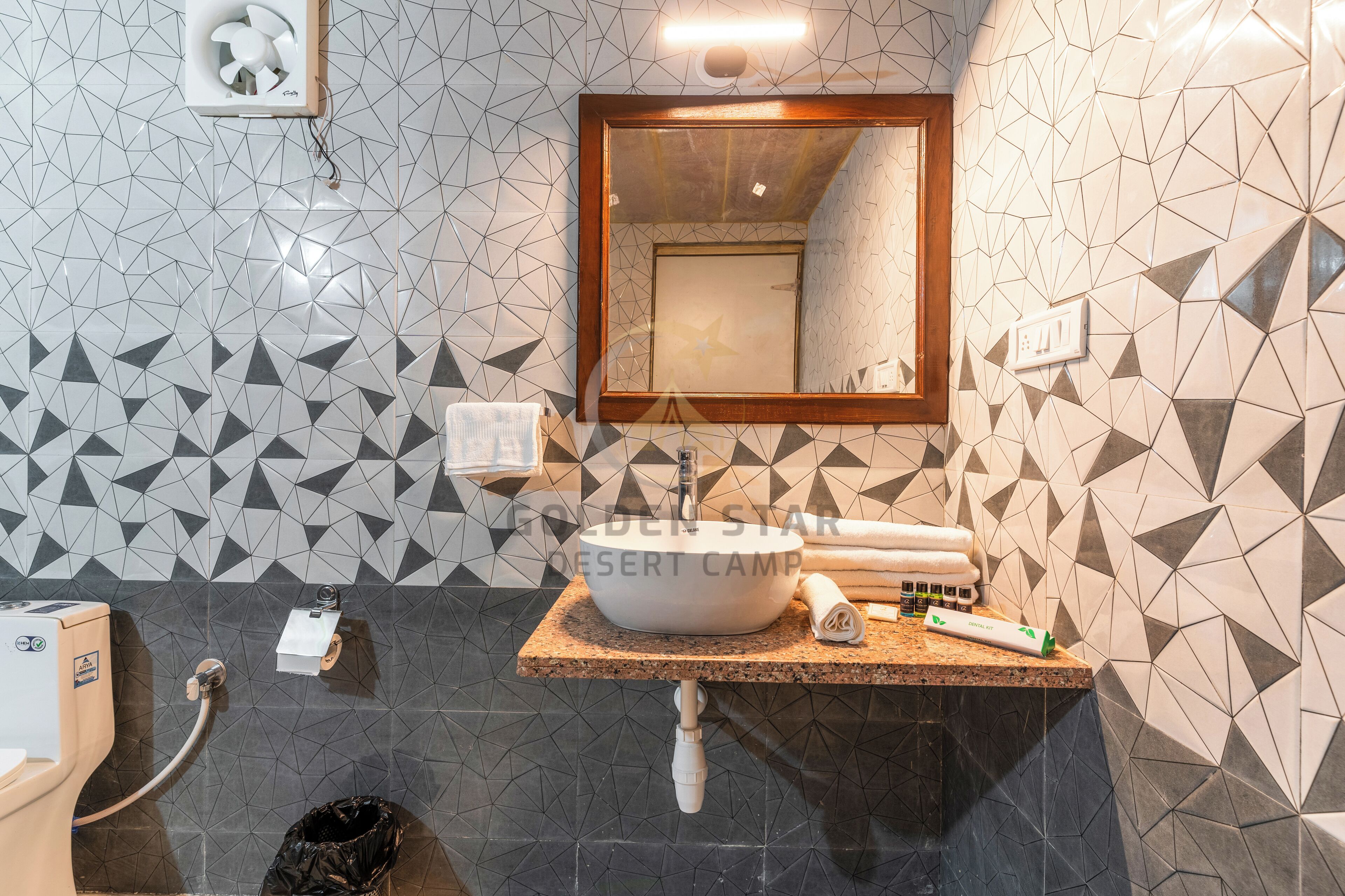 Un baño con un respuesto de azulejos geométricos, un lavamanos con un espejo encima y un perchero.