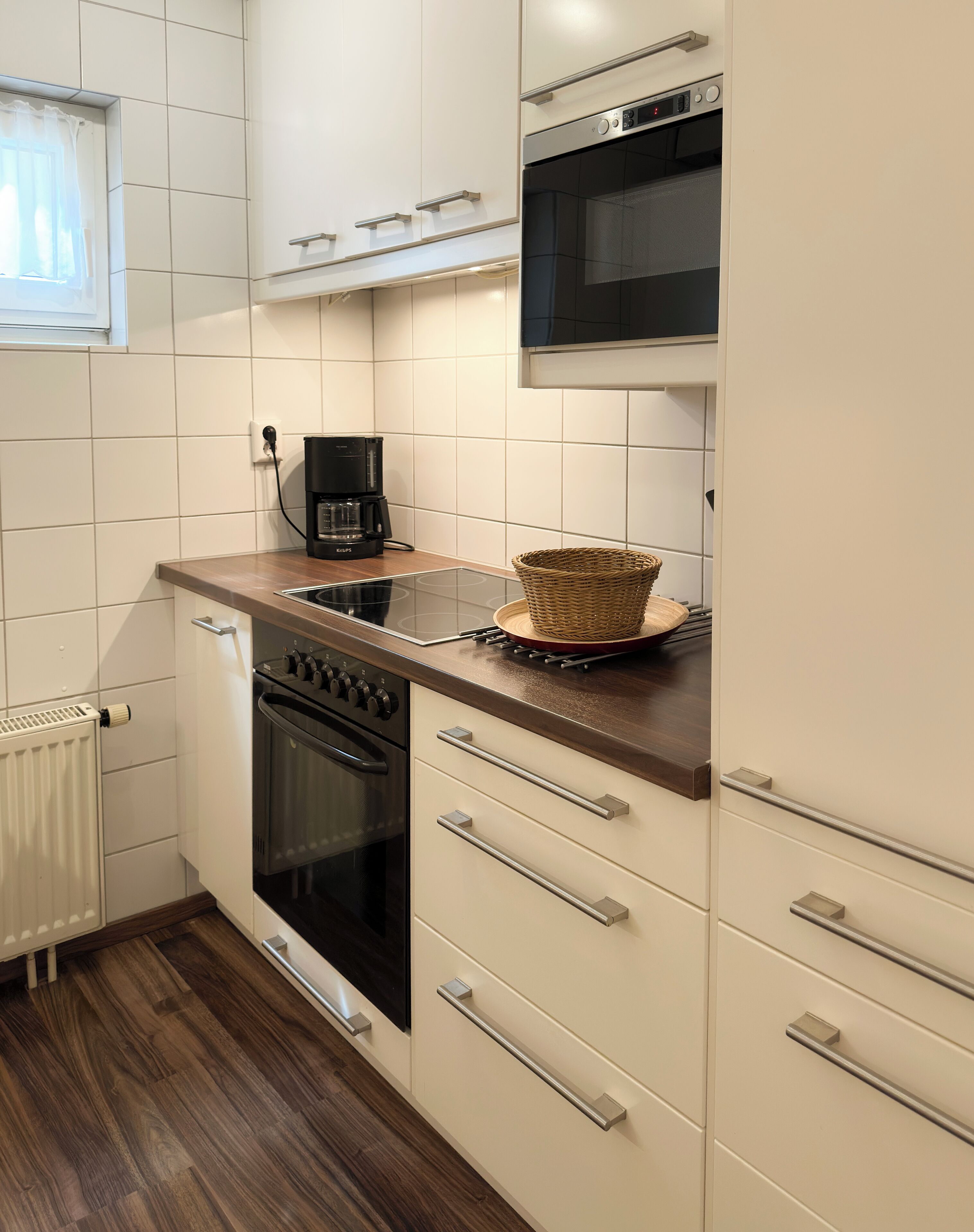 A compact kitchen with white cabinets, a black oven, a coffee maker, and a microwave.