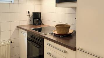 A compact kitchen with white cabinets, a black oven, a coffee maker, and a microwave.