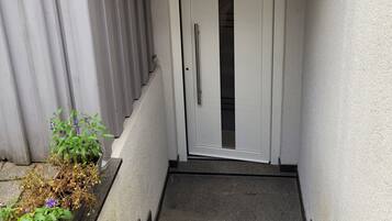 Una escalera estrecha que conduce a una puerta blanca con manija, flanqueada por barandas metálicas y una pequeña maceta con flores.