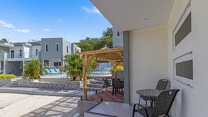 Un espacio al aire libre cubierto con mesa y sillas, piscina y un edificio con balcones.