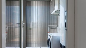 Lavandería con lavadora, tendedero y conducto de ventilación.