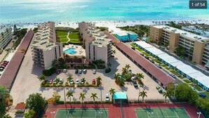 Un hôtel comprenant plusieurs bâtiments, une piscine centrale, des courts de tennis et offrant une vue sur la plage.
