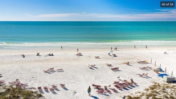 Une plage bordée de rangées de chaises longues et de parasols, un ciel bleu azur et l’océan en toile de fond.