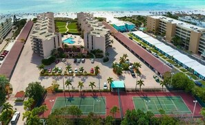 A hotel with multiple buildings, a central pool, tennis courts, and a beach view.