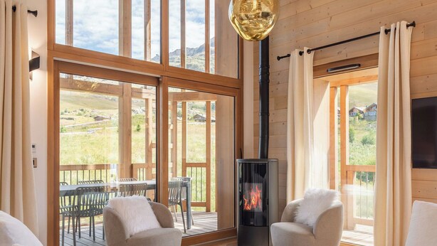 A spacious living room with large windows, a fireplace, and a modern chandelier.