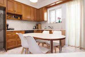 A kitchen with wooden cabinets, a dining table with chairs, a window with curtains, and a countertop with various appliances. - Spacious 3 Bd House in Alimos Athens Riviera (Alimos)