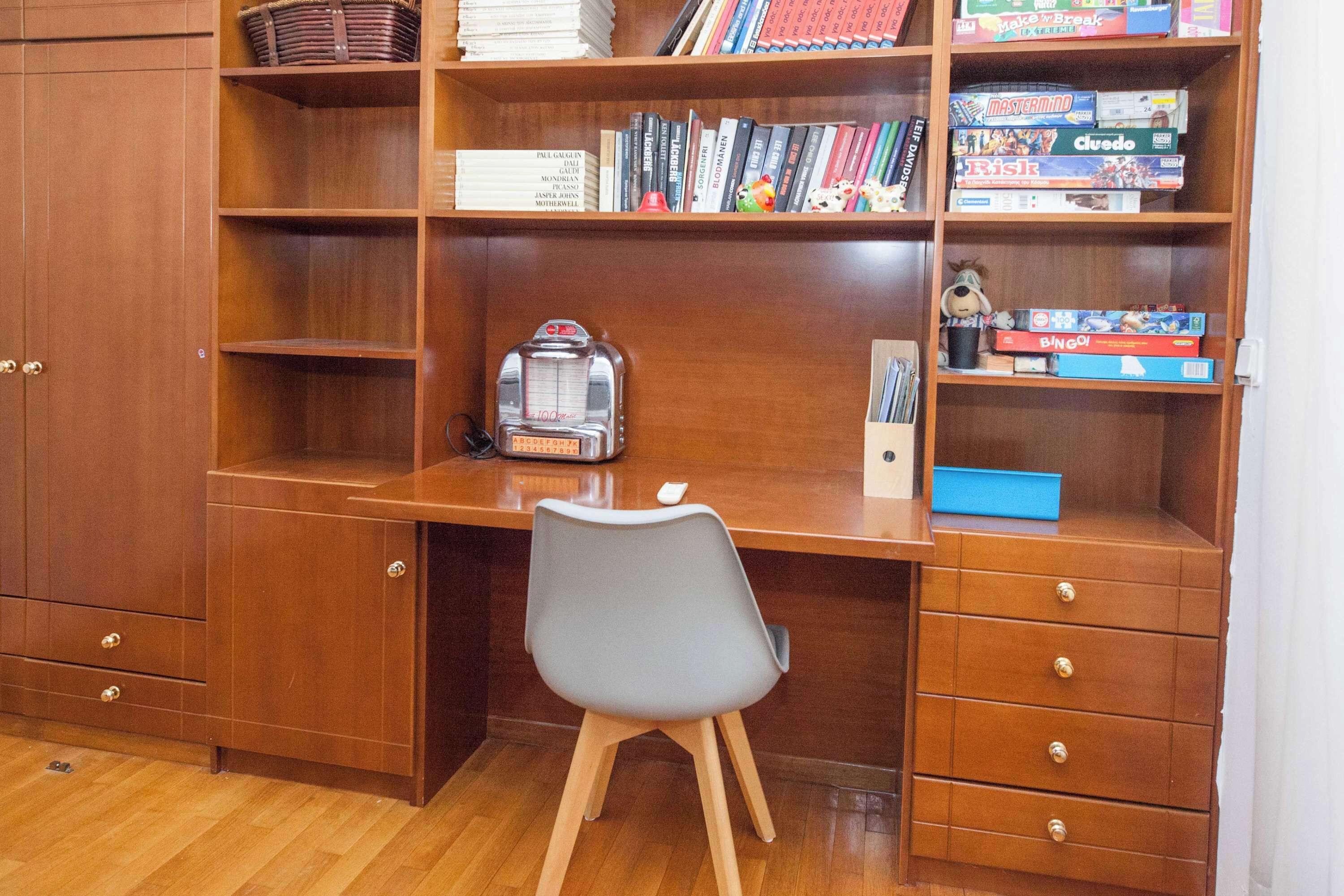 Un escritorio de madera con una silla, una estantería con diversos objetos y un pequeño estante con un juguete.