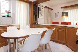 A modern kitchen with a round dining table, white chairs, wooden cabinets, and a pendant light. - Spacious 3 Bd House in Alimos Athens Riviera (Alimos)