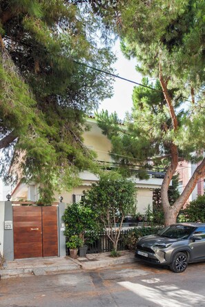 Un edificio residencial con un portón de madera, un coche aparcado y un árbol grande al frente.