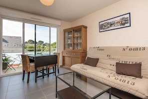 Un salon comprenant un canapé, une table basse en verre, une table à manger avec des chaises, un meuble et une grande fenêtre.