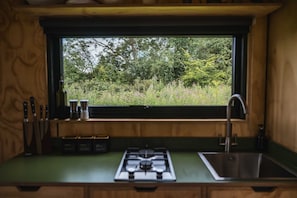 A kitchen with a window view of a forest, a gas stove, and a sink. - Eco Off-Grid Hideaway with Scenic Walks (Tarporley)