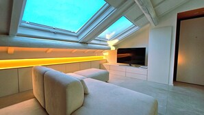 A modern living room with a large flat-screen TV, built-in seating, and skylights. - The Attic Room on Niella Street, in the city center and near the sea (Savona)