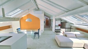 A spacious loft with high ceilings, skylights, a dining area, and a living space with a sofa and cushions. - The Attic Room on Niella Street, in the city center and near the sea (Savona)