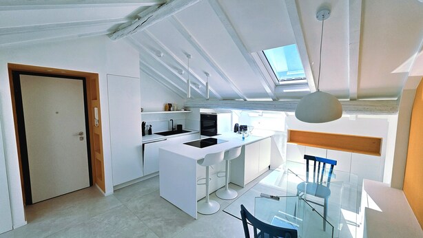 A modern kitchen with a central island, a dining area with a glass table, and a skylight above. - The Attic Room on Niella Street, in the city center and near the sea (Savona)