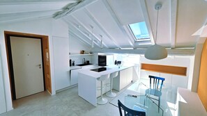 A modern kitchen with a central island, a dining area with a glass table, and a skylight above. - The Attic Room on Niella Street, in the city center and near the sea (Savona)
