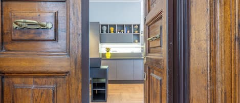 A wooden door with a brass handle leading to a kitchen with grey cabinets and a black countertop.