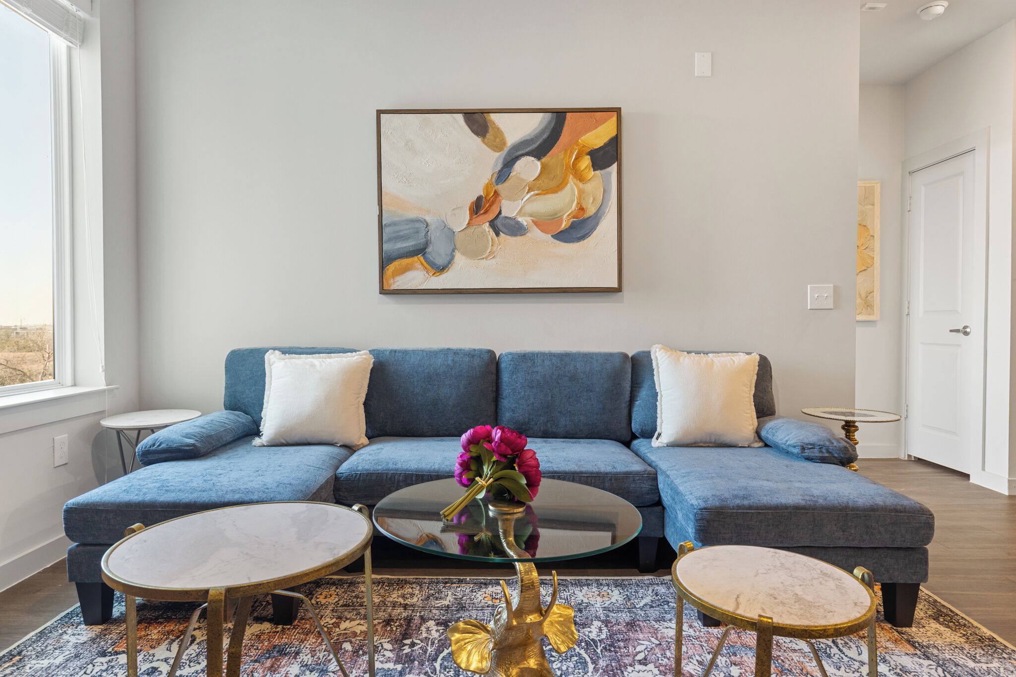 A modern living room with a blue sofa, two round tables, and a large abstract painting on the wall.
