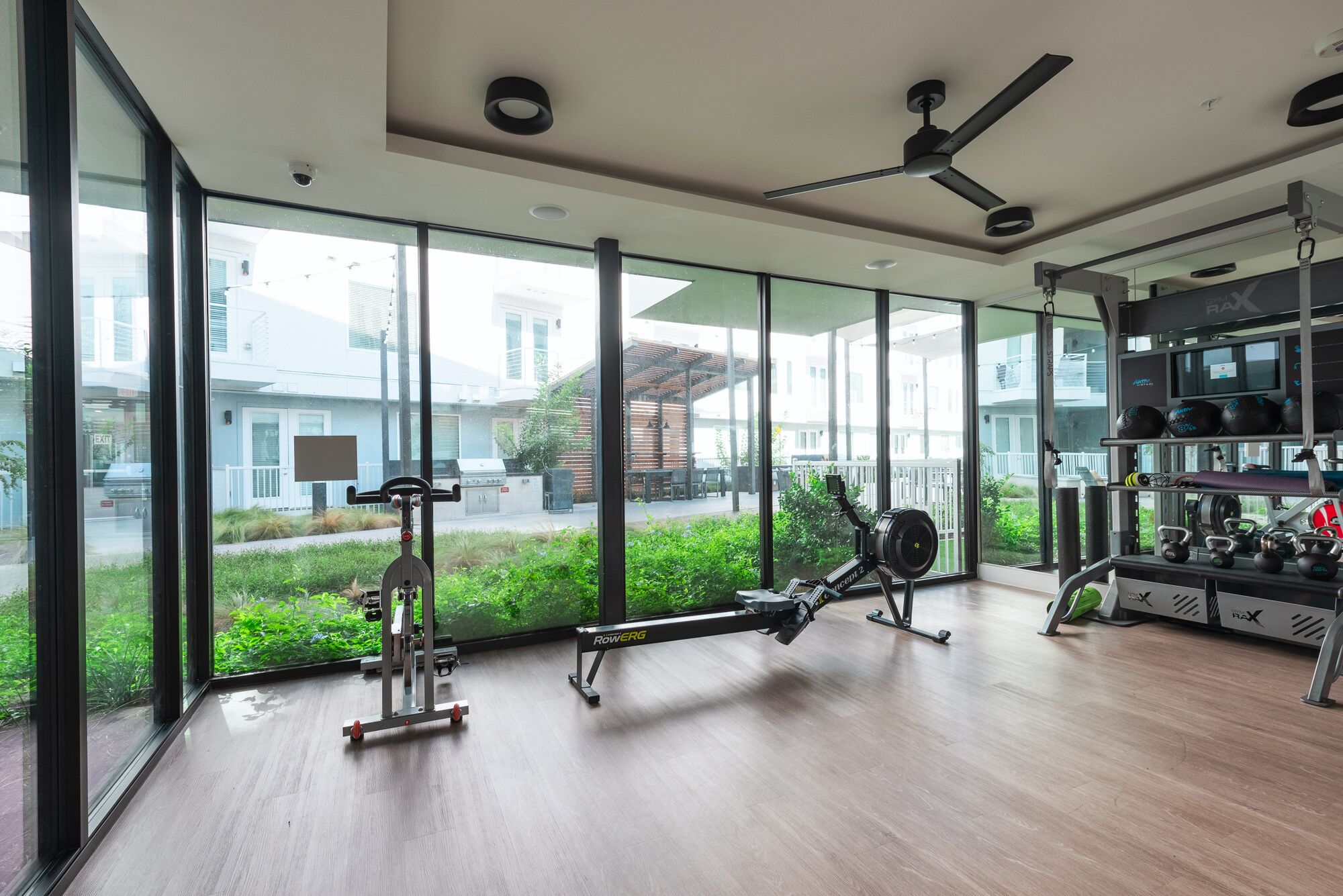 Une salle de sport moderne dotée de grandes fenêtres, d’équipements d’exercice et d’un ventilateur de plafond.