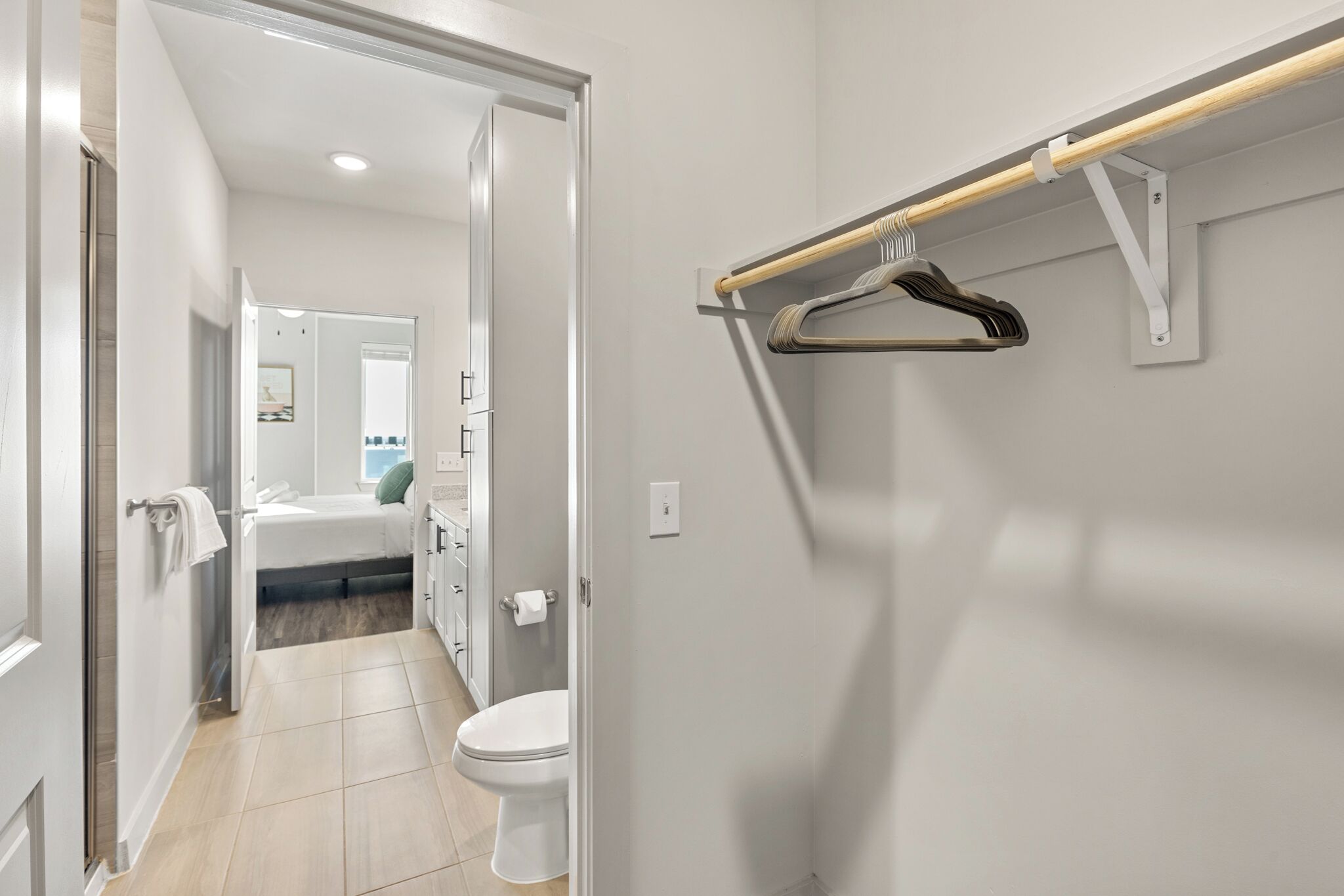 Et moderne badeværelse med toilet, bruseområde og en seng i baggrunden.