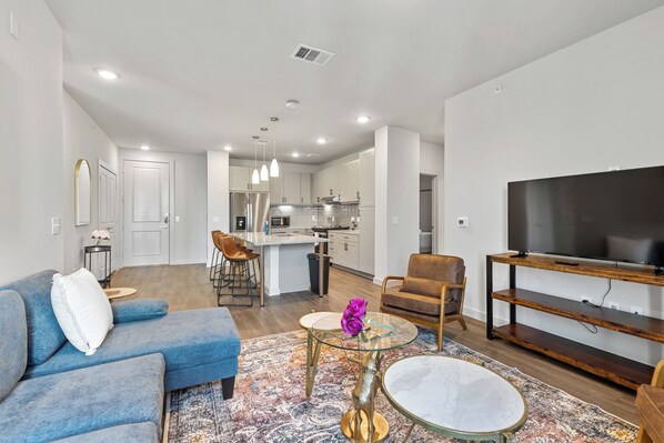 A modern living room with a blue sofa, a glass coffee table, and a TV stand.