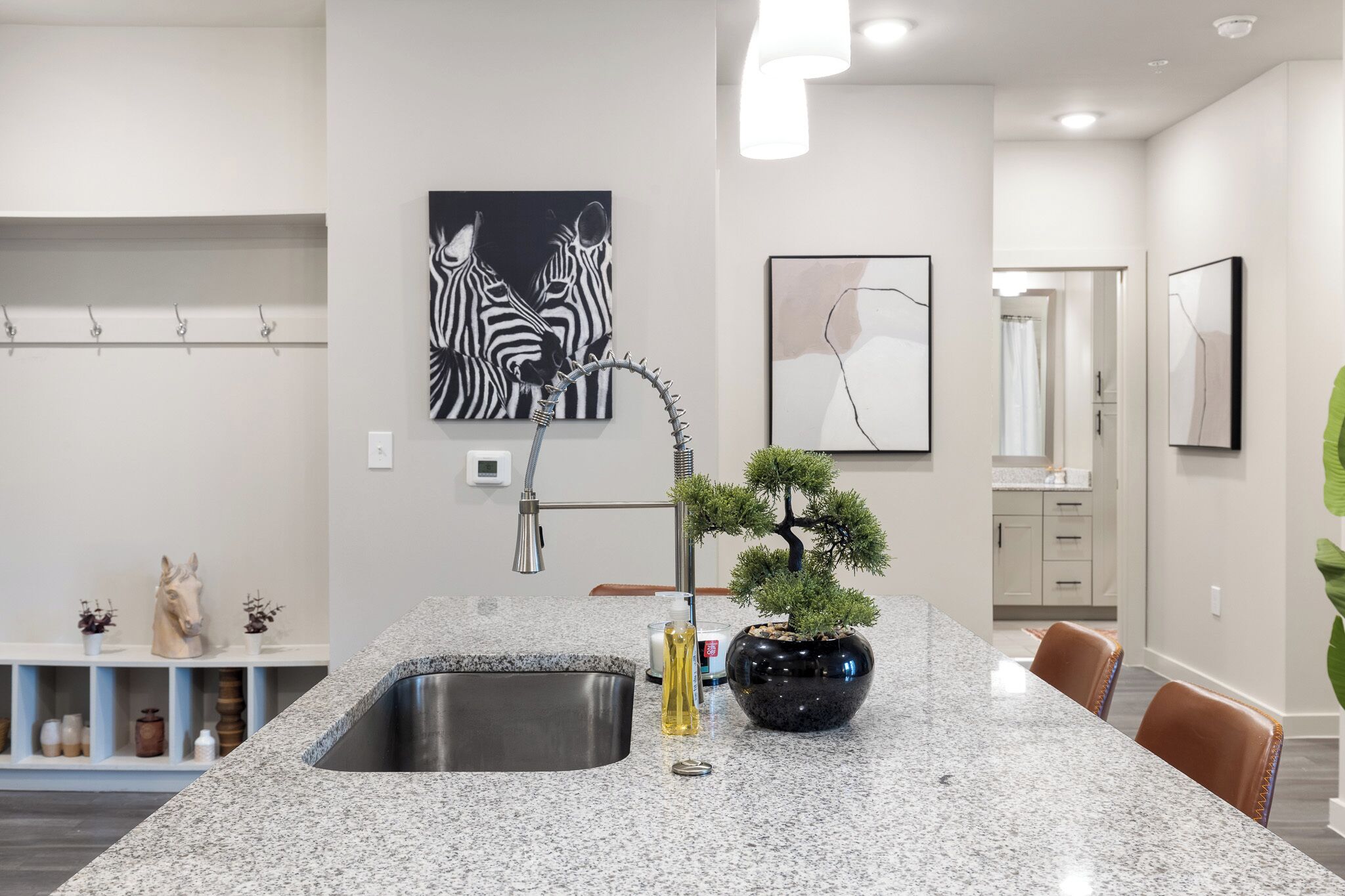 A kitchen with granite countertops, a sink, a vase with a plant, and artwork on the walls.