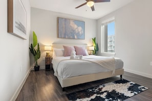 Camera da letto con un letto, lampade da comodino, ventilatore a soffitto, una finestra e vista sugli edifici.