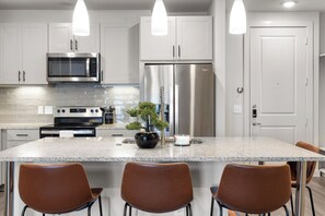 Una cucina moderna con elettrodomestici in acciaio inossidabile, un piano di lavoro in granito e tre sedie marroni.