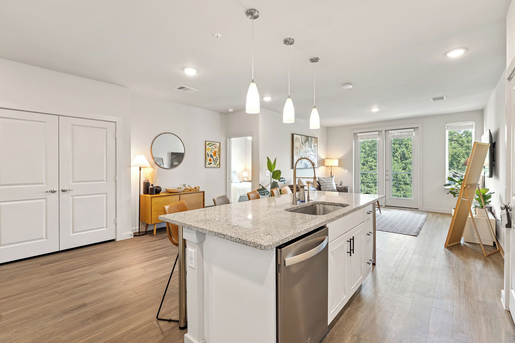 A modern kitchen with a granite countertop, stainless steel appliances, pendant lighting, and large windows offering natural light.