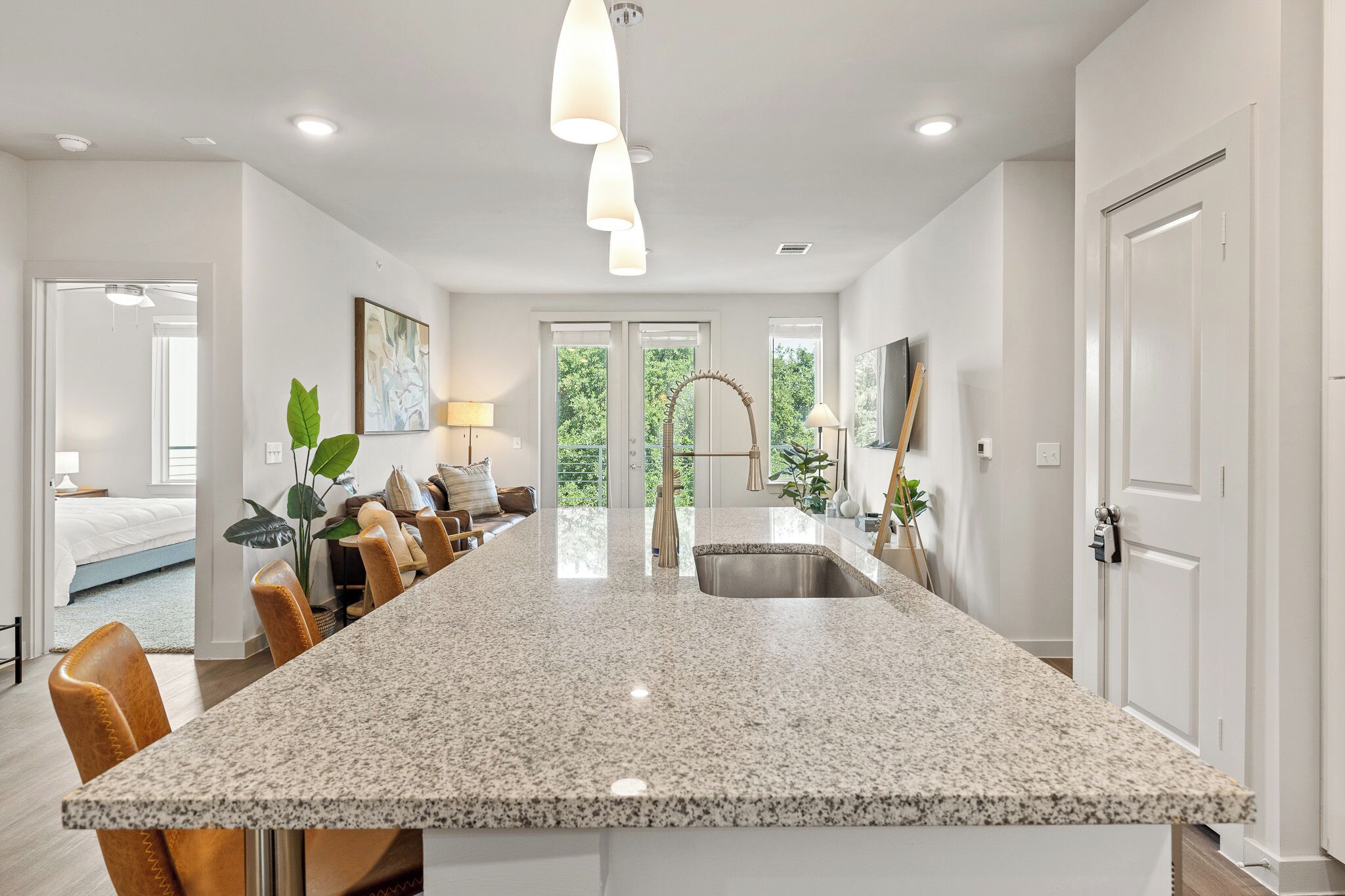 A modern kitchen with a large granite island, stainless steel sink, and pendant lighting.