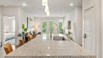 A modern kitchen with a large granite island, stainless steel sink, and pendant lighting.