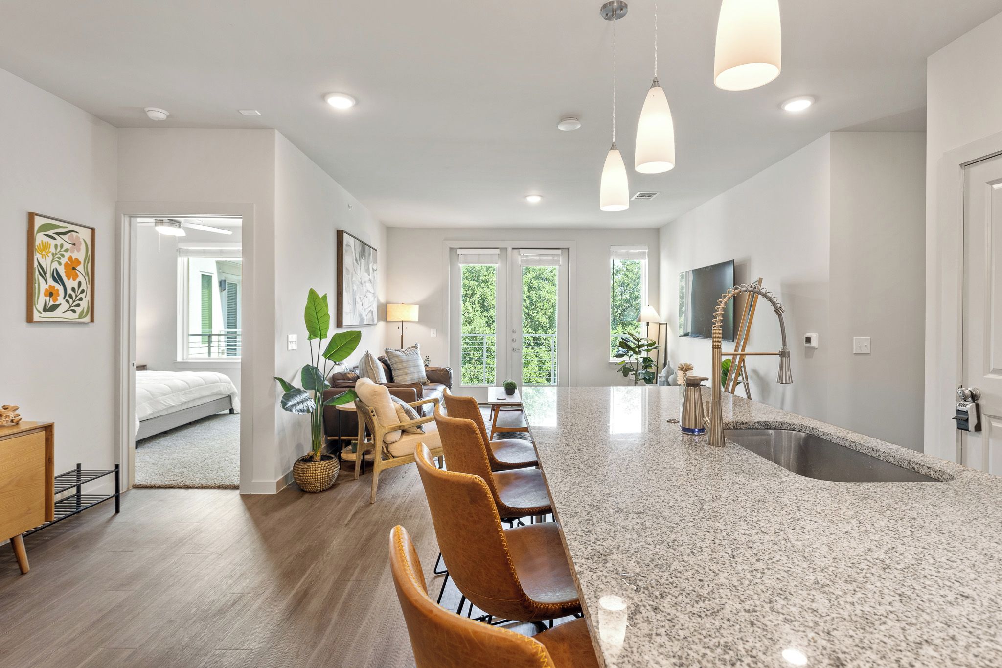 A spacious kitchen with a granite countertop and a large sink. There is a dining area with a long table and chairs, and a living room with a sofa and a coffee table.