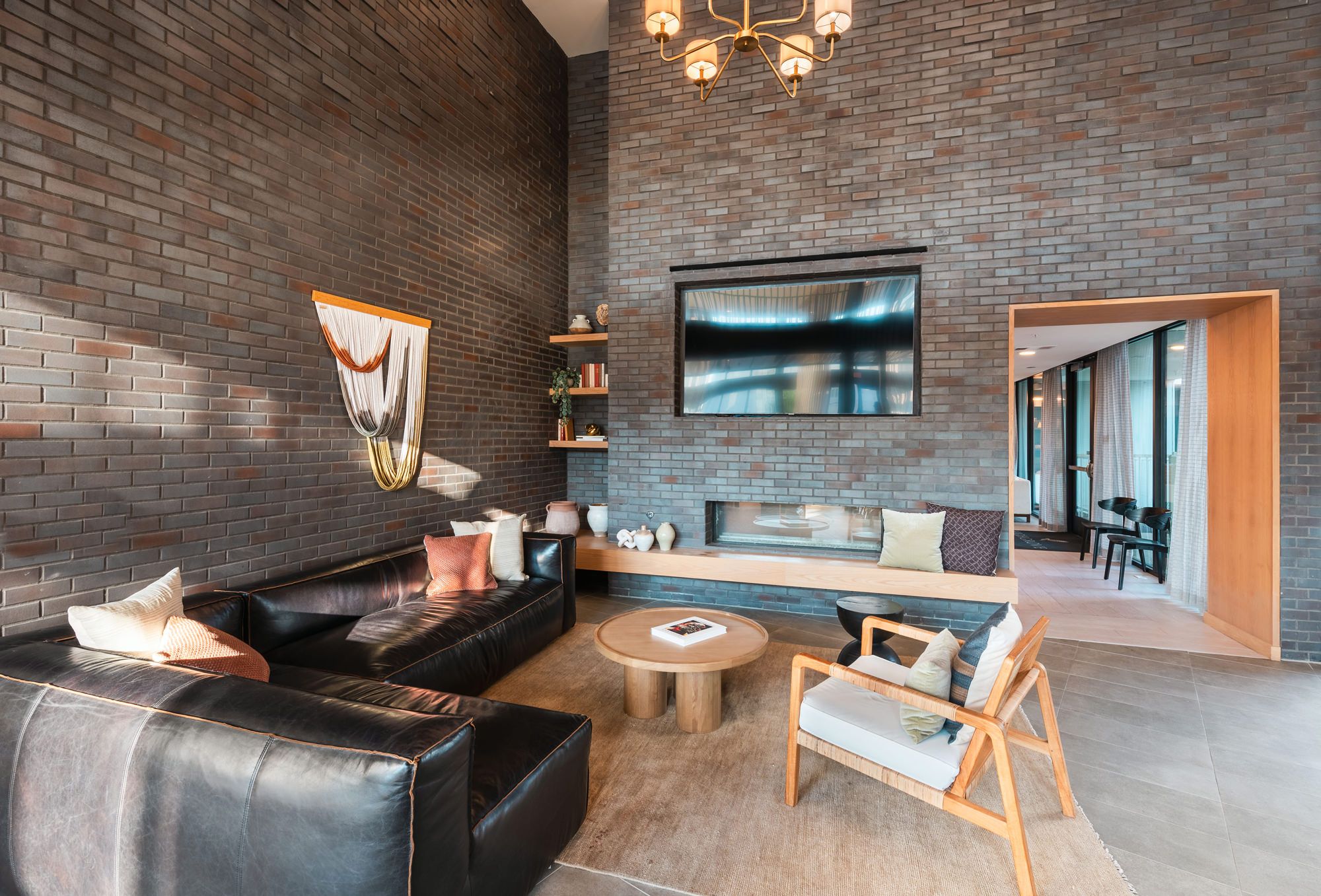 A modern living room with a brick wall, leather sofa, wooden coffee table, and a flat-screen TV mounted above a fireplace.