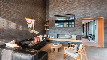 A modern living room with a brick wall, leather sofa, wooden coffee table, and a flat-screen TV mounted above a fireplace.