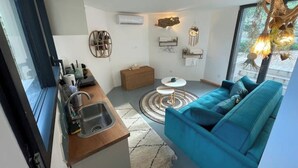 A modern kitchen with a sink, a wooden counter, and a window. There is a blue sofa with cushions and a small round table with chairs. - Relaxation bubble with Jacuzzi (Saint-Martin-de-Londres)