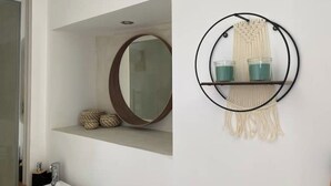 A bathroom with a round mirror, a shelf with decorative items, and a macrame wall hanging. - Relaxation bubble with Jacuzzi (Saint-Martin-de-Londres)
