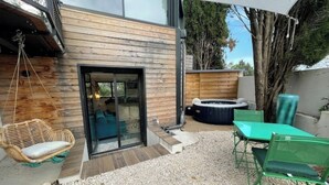 A modern outdoor patio with a wooden wall, a glass door entrance, a hot tub, and outdoor furniture. - Relaxation bubble with Jacuzzi (Saint-Martin-de-Londres)