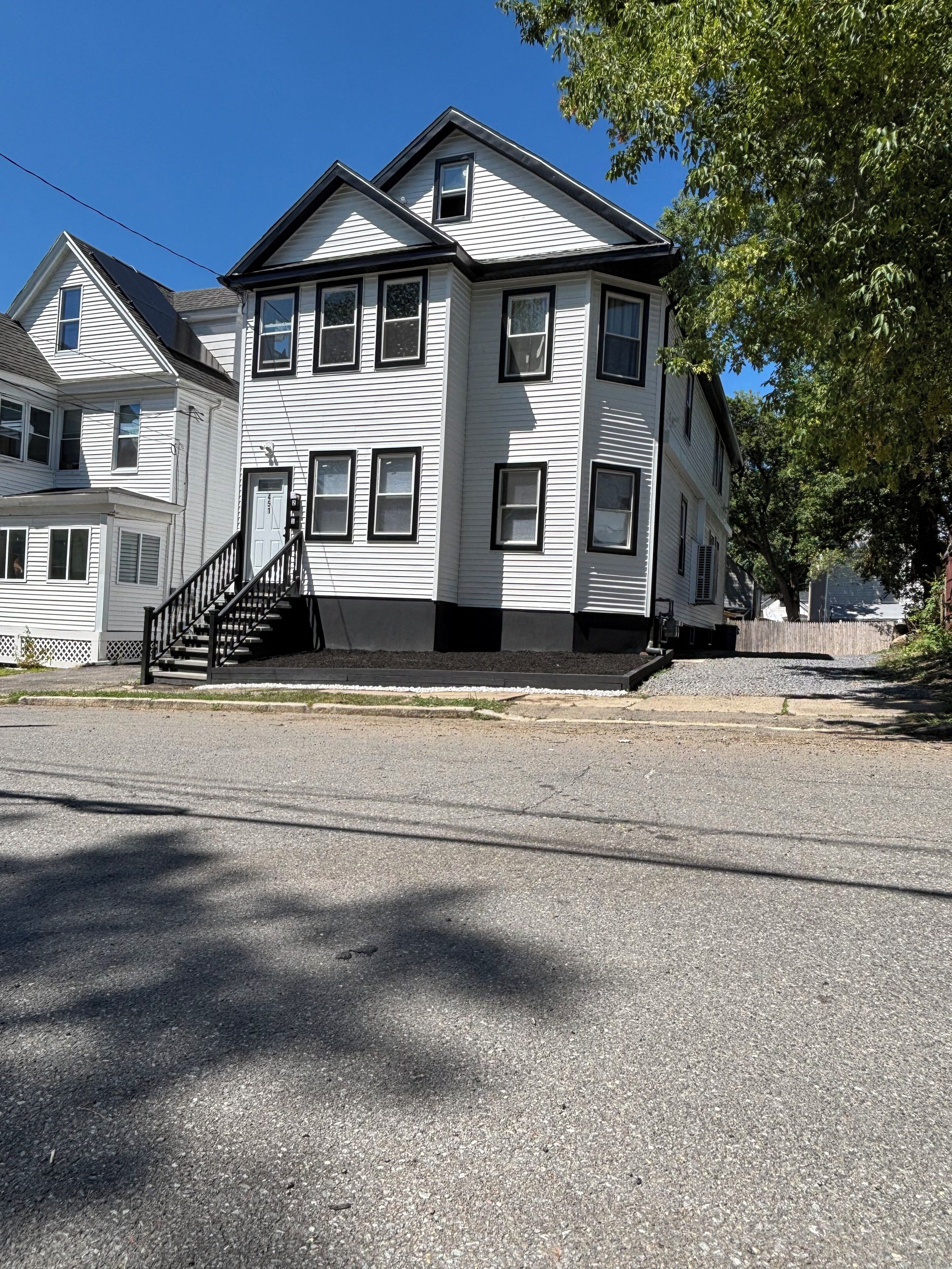 A two-story white building with a black staircase, multiple windows, and a visible front door.