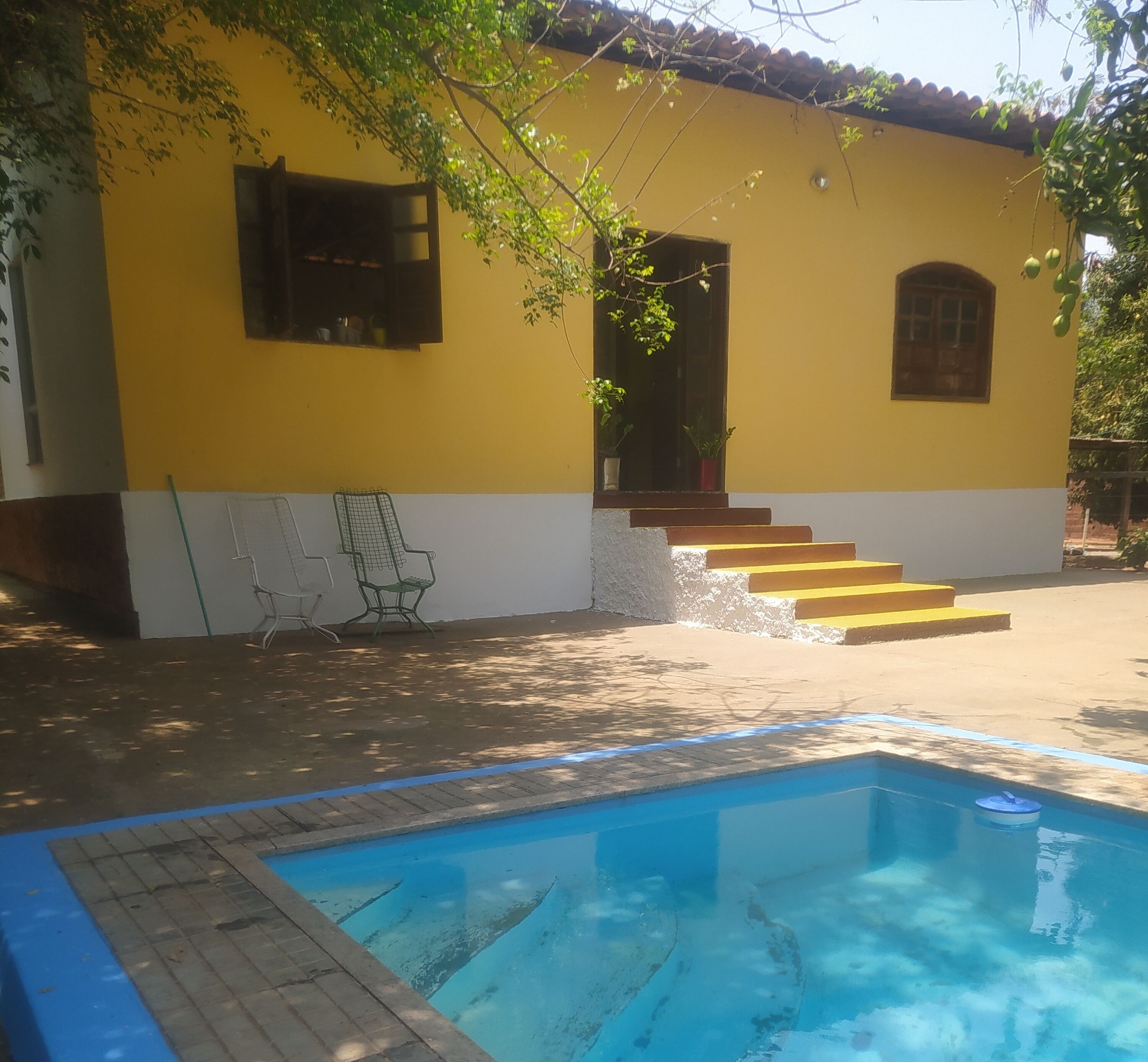 Um edifício amarelo com piscina, degraus que levam à entrada e área de estar ao ar livre.