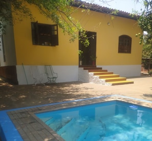 Un bâtiment jaune avec une piscine, des marches menant à l’entrée et des sièges à l’extérieur.