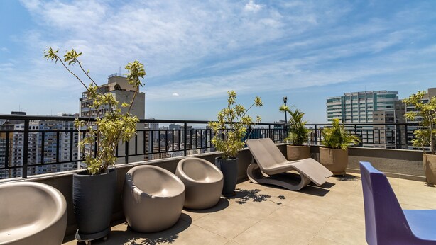 A rooftop terrace with lounge chairs, planters with greenery, and a cityscape view. - Ycp704 in S o Paulo (São Paulo)